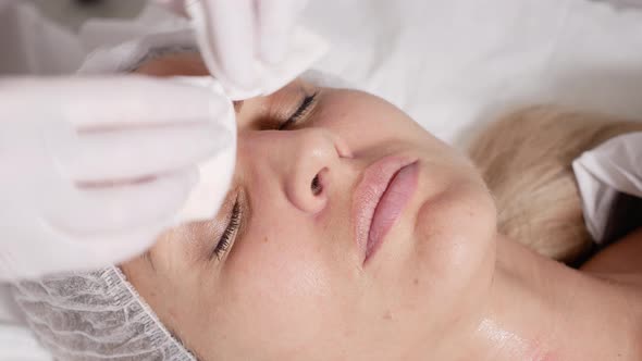 Doctor Beautician Removes Makeup Patient Lying on a Special Table