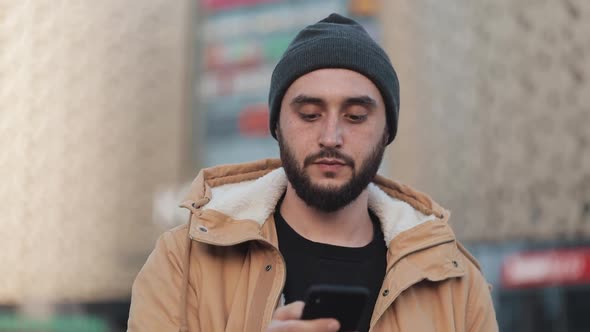 Happy Young Beard Man Using Smartphone Walking in the Street Near Shopping Mall