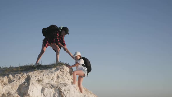 Girl Helps Her Friend Climb Up the Last Section of Mountain. Tourists with Backpacks Help Each Other