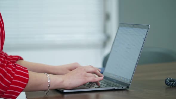 Woman using laptop indoor. Close up of woman working at home office, hand on keyboard