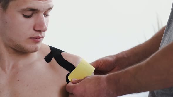 Osteopath Doing Kinesiology Taping on Patient's Shoulder in Clinic