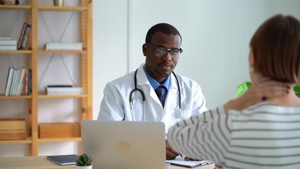 Young Male African Doctor Talking to Patient About Disease During Therapy in Modern Clinic Spbas