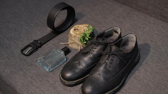 Wedding Details of Groom. Bridegrooms Perfume, Belt, Shoes and Wedding Rings Lie on Sofa