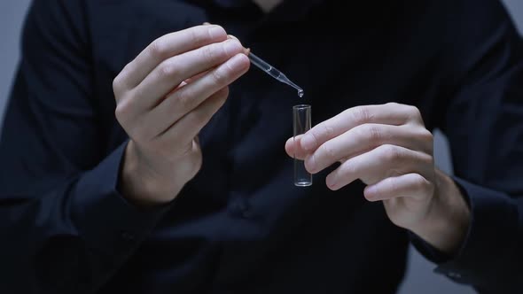 Man Holds a Pipette and a Test Tube in His Hands and Drops One Drop of the Solution Into the Test