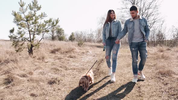 Young Man and Woman in Denim Are Walking in the Wheat Field with a Dog