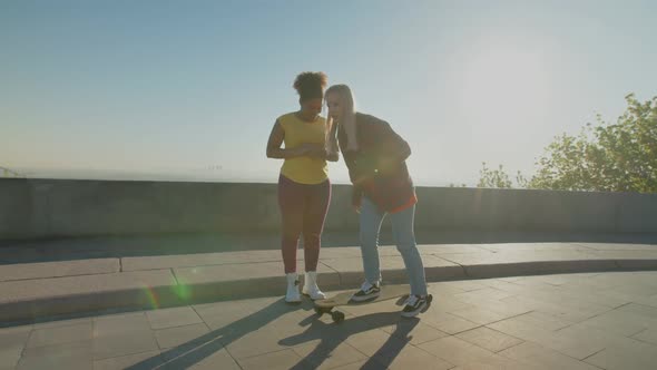 Skillful Woman Teaching Black Female Skateboarding Outdoors at Dawn