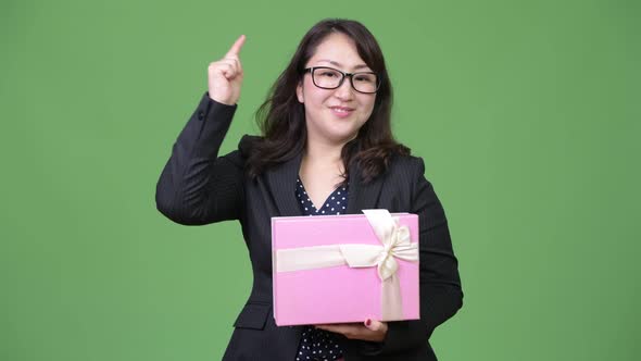 Mature Beautiful Asian Businesswoman Holding Gift Box and Pointing To Camera