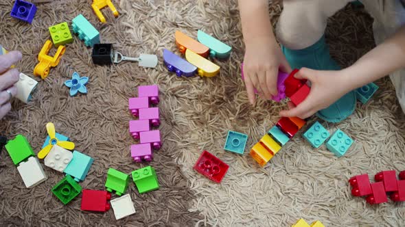 the Hands of a Child and the Hands of an Adult Assemble Multicolored Plastic Blocks of a Children's