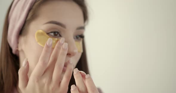 Woman Applying Hydrogel Undereye Recovery Patches on a Light Background