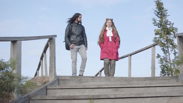 Young Middle Eastern Man and Caucasian Woman in Casual Clothes Going Down the Stairs in Autumn Park
