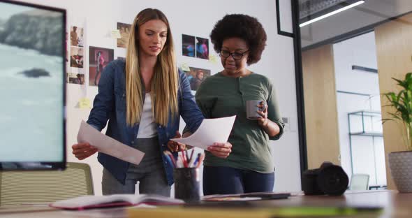 Two diverse female colleagues discussing and looking at images standing in office