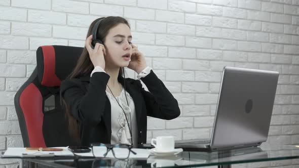 Business girl at the computer puts on headphones.