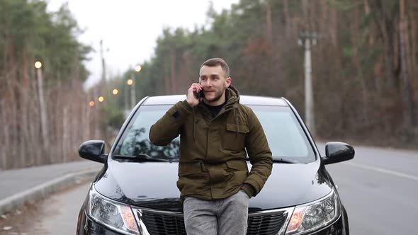 Man leaning on the hood of a car, typing on the phone