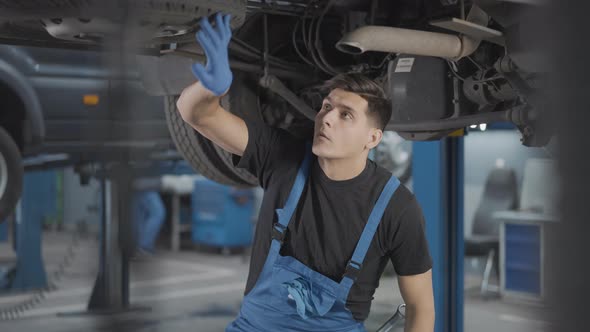 Professional Brunette Service Man Examining Auto Parts Under Vehicle