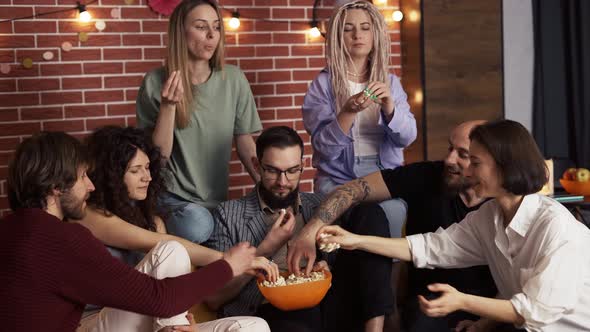 Friends Grabbing Popcorn From a Bowl While Sitting on a Sofa at Home