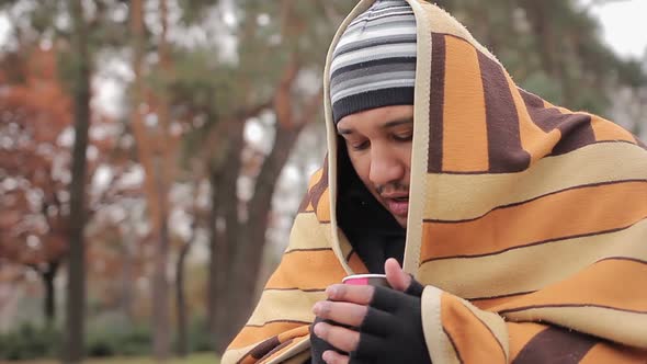 Poor Man With Sad Face Hiding From Cold in Shabby Blanket, Warming With Hot Tea