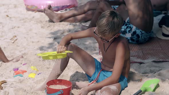 Boy in Blue Swimming Trunks Sows Sand Through Sieve on Beach