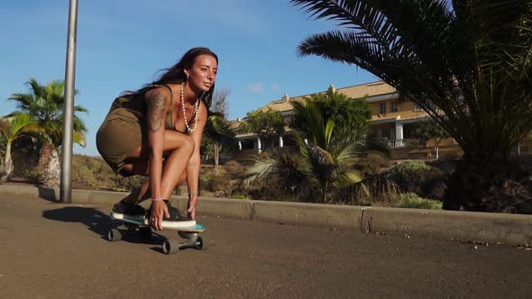 A Young Woman in the Summer Riding a Longboard Near the Palm Trees in Shorts and Sneakers