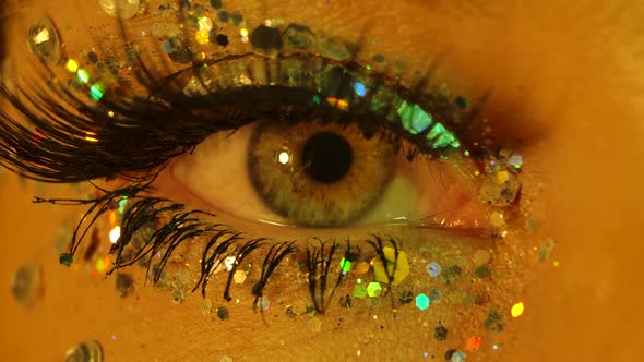 A Woman Opens Her Eye with Long Eyelashes and Sparkles Illuminated By Yellow Green Neon Lights