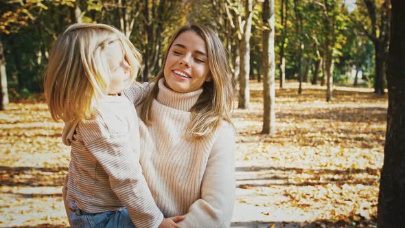 Young Blonde Mom Smiling Holding Little Child Girl in Arms and Circling with Her During Their Walk