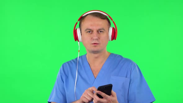 Medical Man in Big Red Headphones Turns on Music at Mobile Phone. Green Screen