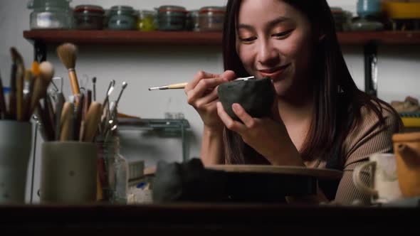 A female ceramicist is creating a new pottery in the workshop. Asian woman is enjoying pottery work.