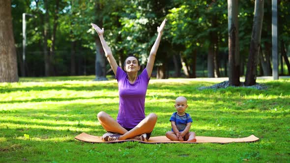 Mother and baby practicing yoga on green grass in park