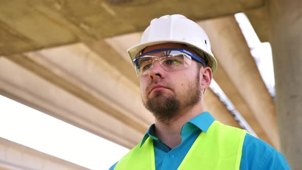 Closeup Portrait of a Young Master Builder in a Protective Helmet at a Construction Site