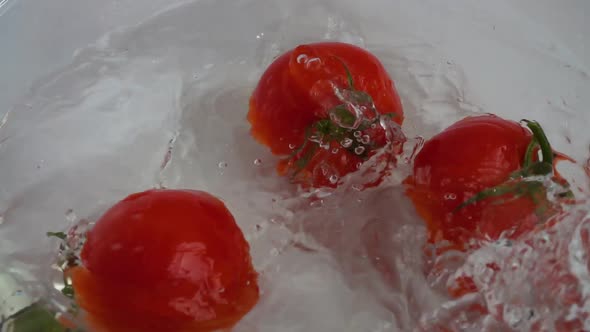 Falling tomatoes in a glass bowl of water. Slow motion.