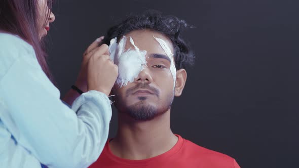 Make up artist putting white insert on man's eye to make a Halloween mask for party