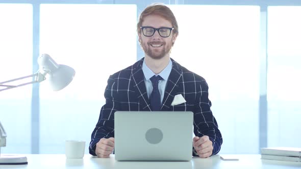 Redhead Businessman Smiling Toward Camera While Working on Laptop