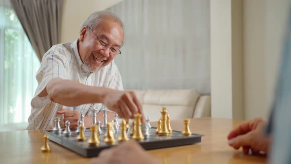 Happy smiling Asian senior older man enjoy activity in house playing chess game with friend together