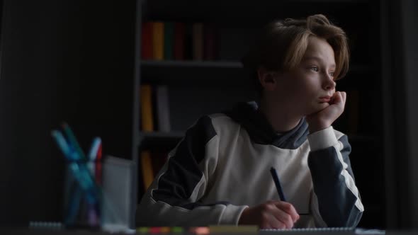 Portrait of Pupil Boy Looking at Laptop Screen During Online Lesson and Taking Notes in Copybook