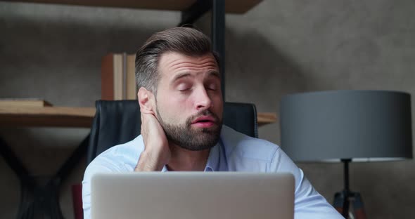 Front View of a Tired Caucasian Businessman Working in a Modern Office Sitting at a Desk Looking at