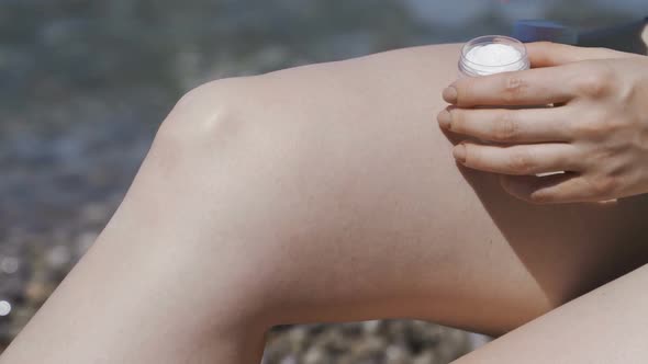 Sunscreen. A Girl Smears Leg with Cream on the Beach.