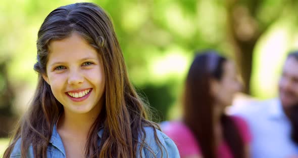 Little girl smiling at camera with family behind on park bench