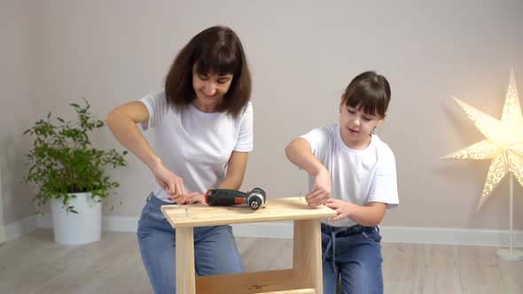 Happy Family Mother and Daughter Assembling Wooden Furniture Together with Screwdriver