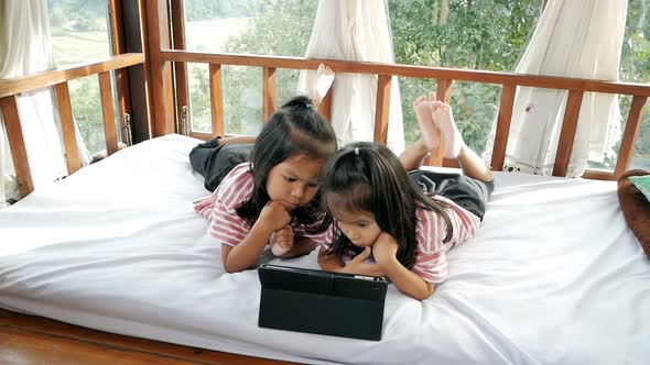 Little girls is looking at tablet on the bed.