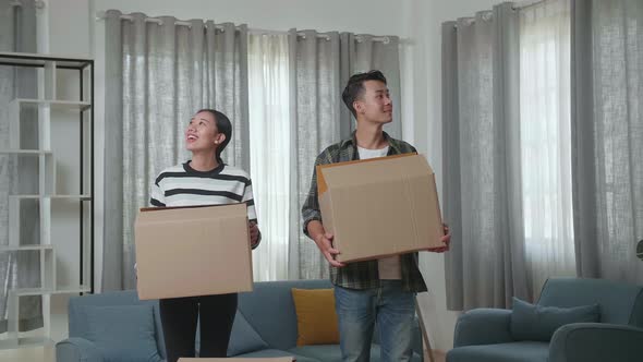 Smiling Young Asian Couple Carrying Cardboard Boxes With Stuff Into A New House Then Looking Around