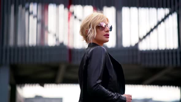 Portrait of a Blonde Woman in Dark Glasses and a Black Leather Jacket. She Goes Against the