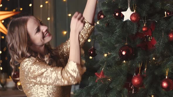 Pretty Young Lady in Elegant Dress Decorating Xmas Tree for New Year's Party