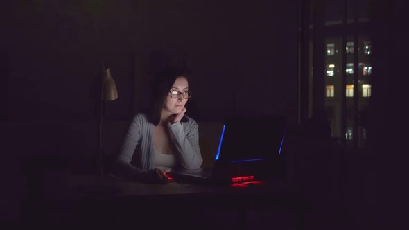 Cute Young Woman Smiling in the Dark Looking at Laptop Screen at Home