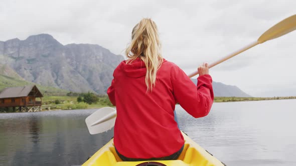 Caucasian woman having a good time on a trip to the mountains, kayaking on a lake, holding a paddle,