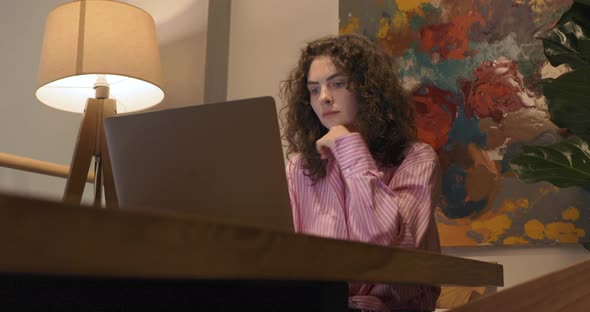 Attractive millennial woman in pink blouse working remotely on modern laptop