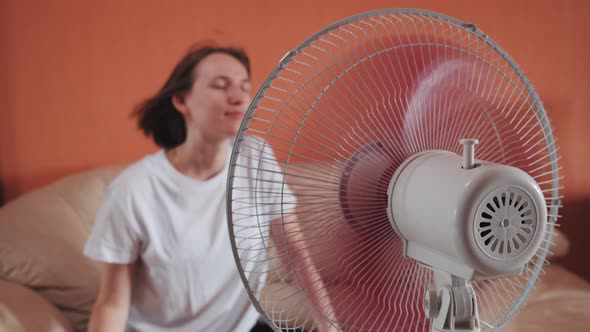 Young Woman Sits in Front of Electric Home Fan Air Stream Blowing Short Hair