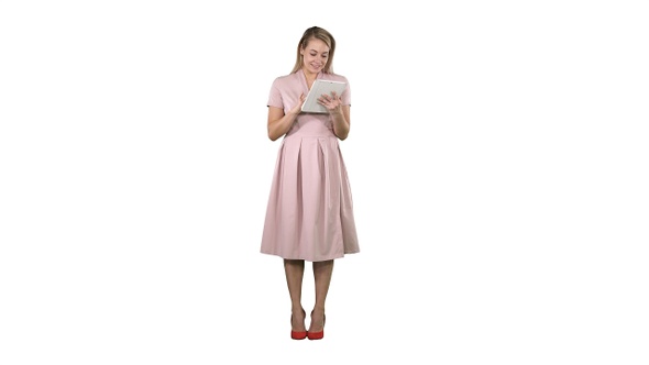 Pretty young woman in pink dress holding tablet and looking