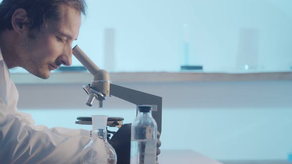 A Male Researcher Looks Into the Eyepiece of a Microscope and Adjusts Its Focus