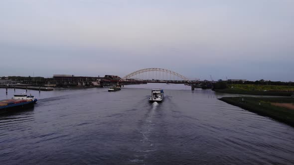 Industrial Barge Cruising At Noord River With Arch Bridge In The Distance. - aerial pullback