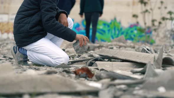 Child plays with stones in front of graffiti.