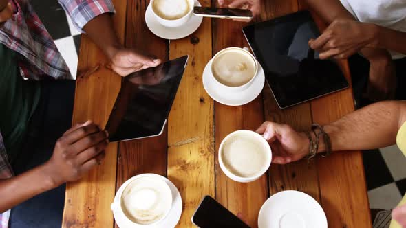 Group of friends using mobile phone and digital tablet while having cup of coffee